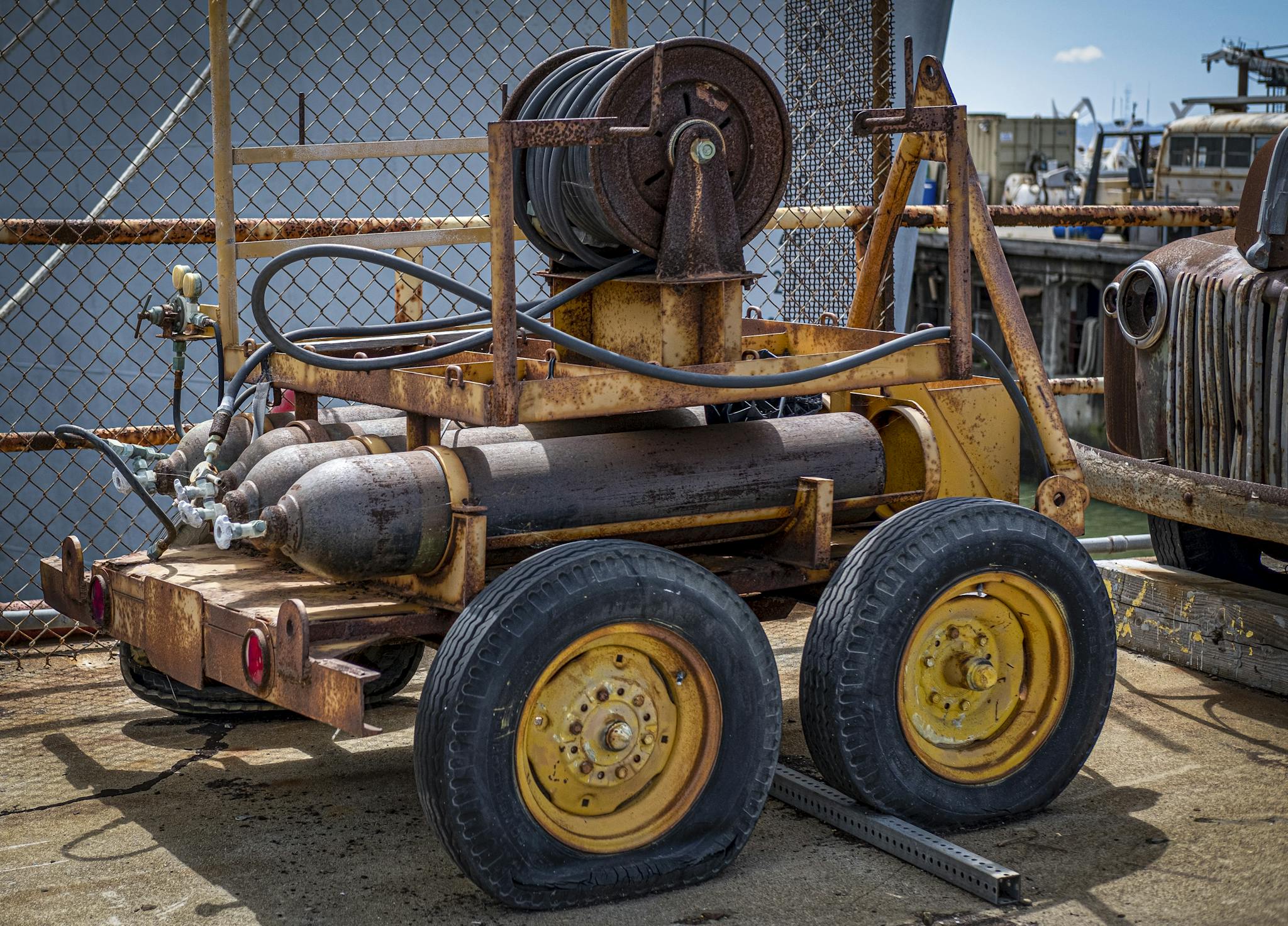 Old rusty industrial cart with hoses and tanks, parked on a sunlit day.
